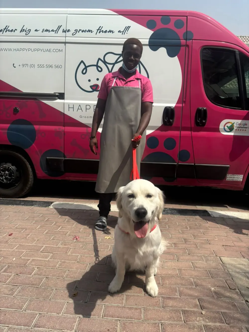 Happy Puppy groomer standing with a golden retriever in front of the grooming van